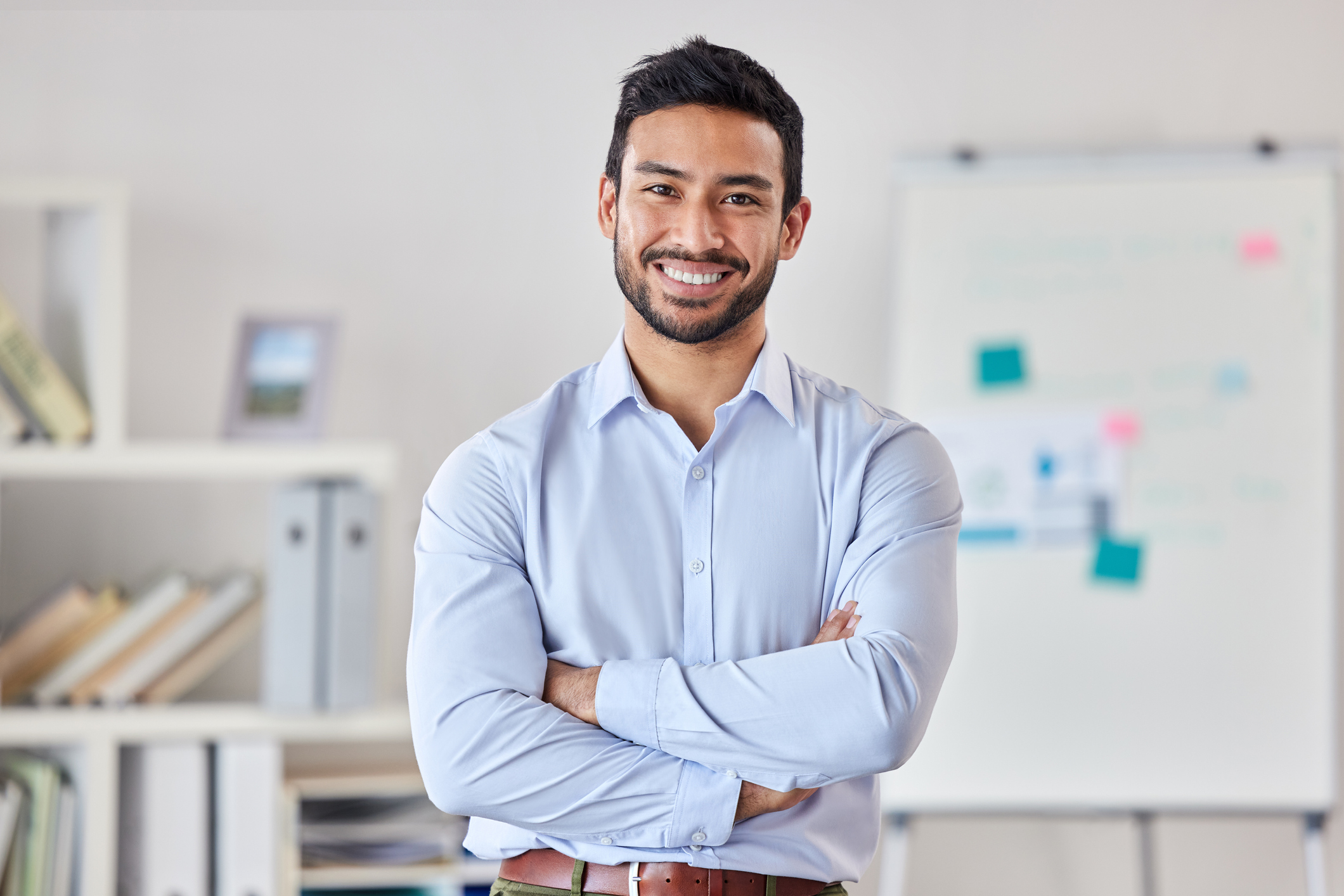 Young happy businessman standing with his arms crossed working alone in an office at work.