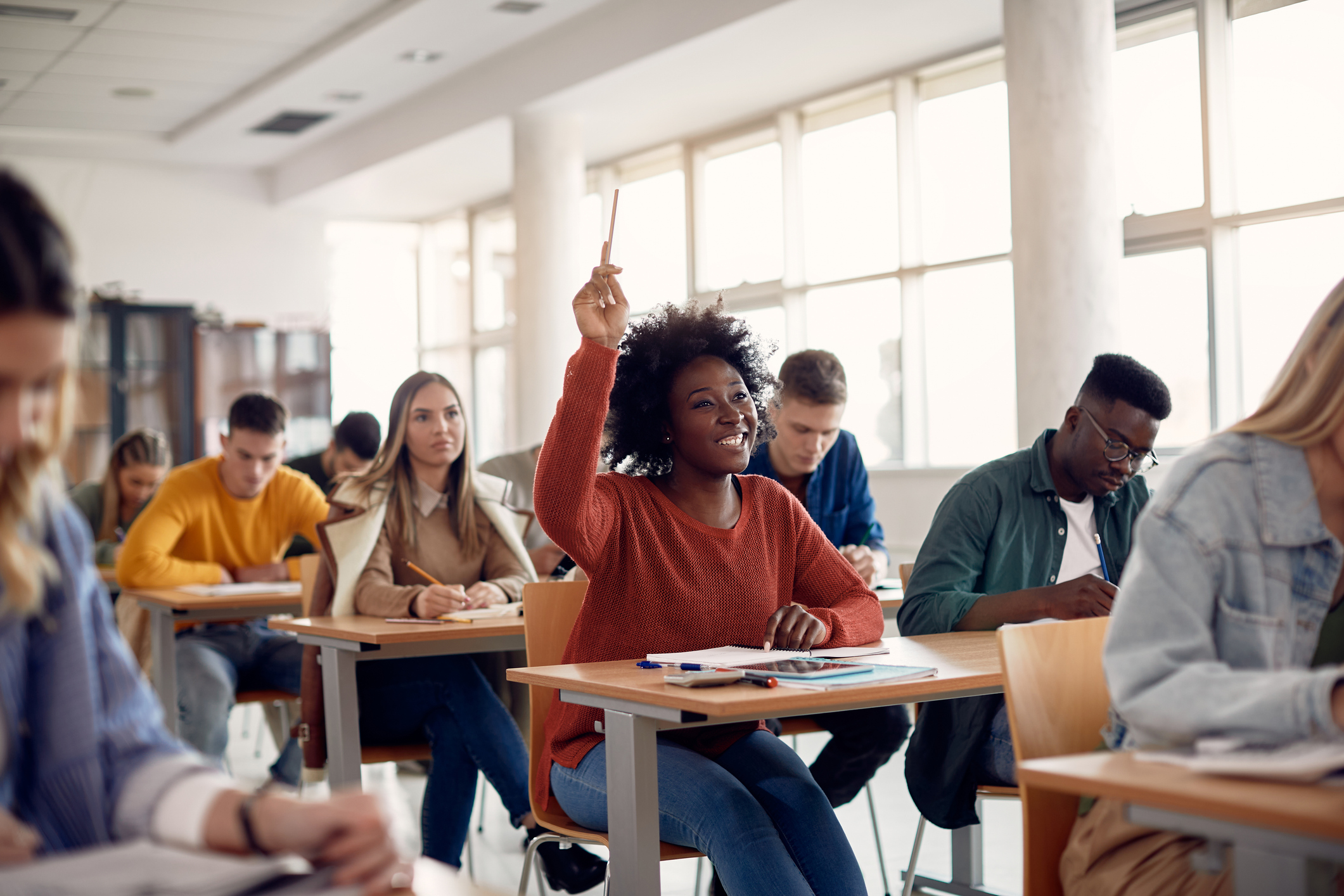 Happy student raising arm to answer question while attending class with her university colleagues.